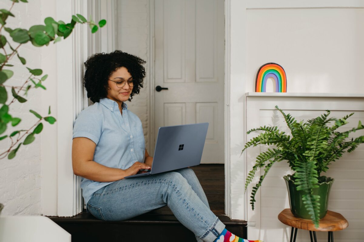 Woman of colour sitting on stairs with open laptop on her knees